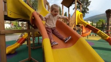 Little girl sticking out her tongue slides down the slide and gets to her feet. High quality 4k footage