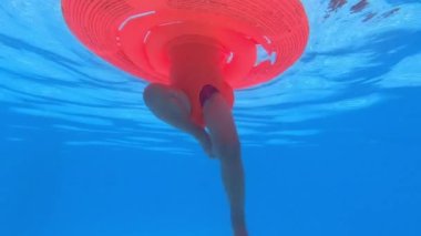 Little girl on an inflatable ring dangles her legs underwater in the pool. High quality 4k footage