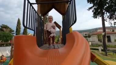 Little girl slides a plush rabbit down a spiral slide on the playground. High quality 4k footage