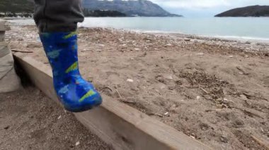Small child in boots gently steps on a narrow board on the beach. High quality 4k footage