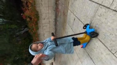 Little girl rides a scooter around the yard, sticking her tongue out, holding her dad hand. High quality 4k footage