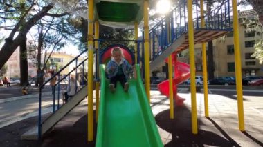 Little girl slides down the slide at the playground. High quality 4k footage