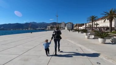 Mom and a little girl run holding hands along the paved embankment. High quality 4k footage
