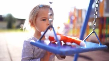 Little girl swings a soft toy on a chain swing on the playground. High quality 4k footage