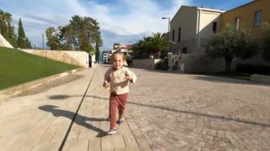 Little girl runs smiling along the tiled pavement in the park. High quality 4k footage