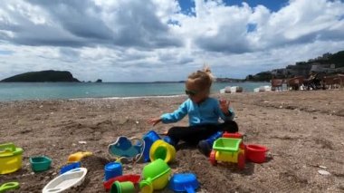 Güneş gözlüklü küçük kız plajda oturur ve plastik kalıplarla oynar. Yüksek kalite 4k görüntü