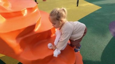 Little girl with a plush rabbit climbs the steps of a slide. High quality 4k footage