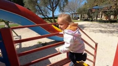 Küçük kız çocuk parkındaki kaydırağın merdivenlerine tırmanıyor, tırabzana tutunarak. Yüksek kalite 4k görüntü