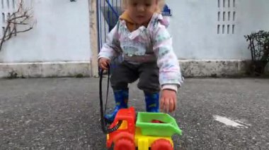 Little girl with a toy car on a string runs along an asphalt road to an apartment building. High quality 4k footage