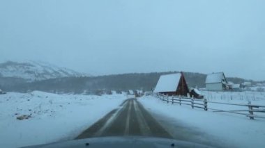 Car drives under the snow on the road of a small town. Zabljak, Montenegro. High quality 4k footage