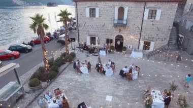 Glowing garlands of light bulbs over laid tables with guests in the yard on the pier. Drone. High quality 4k footage