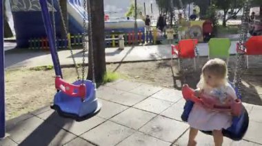 Little girl with a soft toy swings on a chain swing on the playground. High quality 4k footage