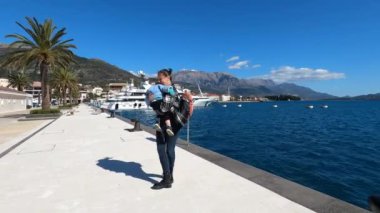 Mother circles a little girl in her arms on a pier by the sea against the backdrop of mountains. High quality 4k footage