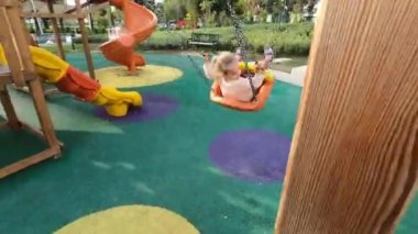 Küçük kız renkli bir oyun kompleksinde sallanıyor. Yüksek kalite 4k görüntü