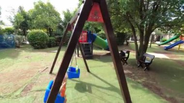 Little girl swings on a chain swing on a playground in the garden near the house. High quality 4k footage