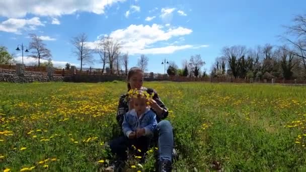 Mom Puts Wreath Yellow Dandelions Head Little Girl Sitting Lawn — Vídeo de Stock