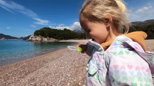 Little Girl Squinting Blowing Soap Bubbles Standing Pebble Beach High — Vídeo de stock