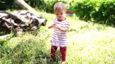 Little girl removes a branch from her way while walking on the lawn. High quality 4k footage