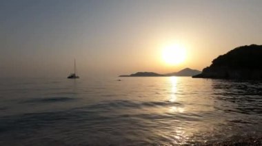 Sailboat in the sea against the backdrop of mountains and the setting sun. High quality 4k footage
