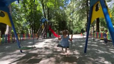 Little girl swings on a chain swing at the playground in the park. Back view. High quality 4k footage