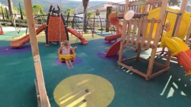 Little girl swings on a chain swing on a wooden playground. High quality 4k footage