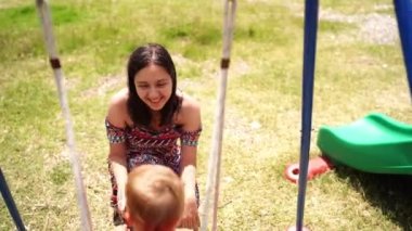 Mom swings a little girl on a swing while squatting next to her. High quality 4k footage