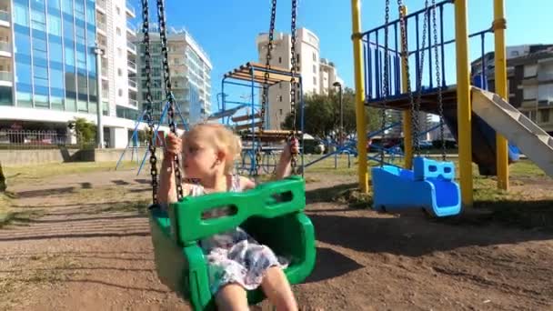 Küçük Kız Yüksek Binaların Yakınındaki Bir Oyun Parkında Zincirli Salıncakta — Stok video
