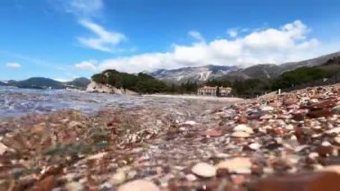 Transparent waves roll over colorful pebbles on a mountainous coast. High quality 4k footage