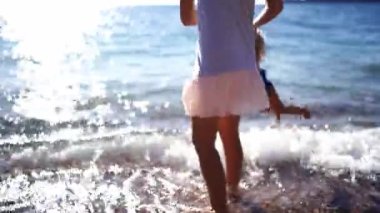 Mom spins a little girl by the arms over the sea surf. High quality 4k footage
