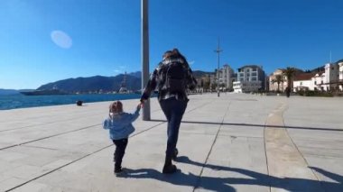 Mom and little girl walk bouncing along the paved embankment. High quality 4k footage