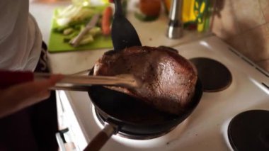 Woman turns steaming roast beef with tongs in a frying pan on a stove. High quality 4k footage