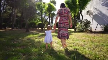 Mom and little girl walk barefoot on green grass in the garden holding hands. High quality 4k footage