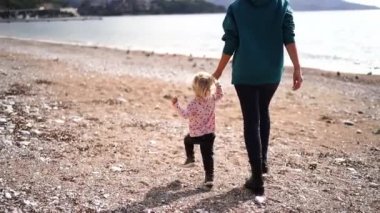Little girl runs along the beach to the sea with her mother by the hand and falls. High quality FullHD footage