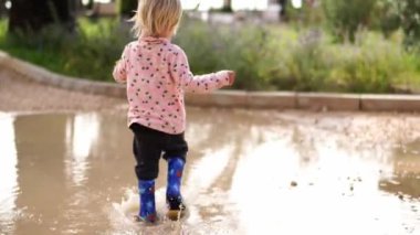 Little girl in rubber boots runs through the puddles in the park. High quality 4k footage