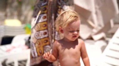 Mom smears sunscreen on the face of a little girl sitting on a sun lounger. High quality 4k footage