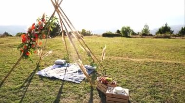 Tipi-style wedding arch stands next to wooden boxes on a green meadow. High quality 4k footage