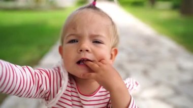 Little girl walks in park and stretches her arms forward. High quality FullHD footage