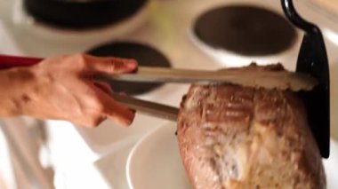 Woman transfers roast beef from a plate to a frying pan with stewed vegetables with tongs. High quality 4k footage