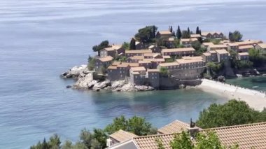 View of the island of Sveti Stefan and the isthmus to it over the red roofs of houses. High quality 4k footage