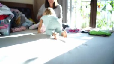 Little girl crawls along the bed to her mother, who folds clean linen after washing into piles. High quality 4k footage