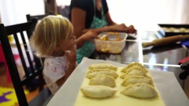 Little girl eats with a spoon the filling for buns that her mother sculpts at the table. High quality 4k footage