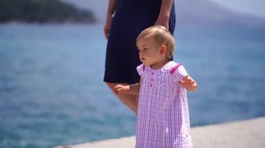 Küçük kız rıhtımda annesinin yanında çıplak ayakla yürüyor, elleriyle dengede duruyor. Yüksek kalite 4k görüntü