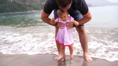 Dad lifts and lowers little girl by the waist into the surf. High quality 4k footage