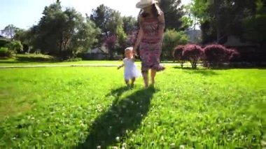 Anne ve küçük bir kız çiçek açan çalıların ve ağaçların arasında yeşil bir çimenlikte yürüyorlar. Yüksek kalite 4k görüntü