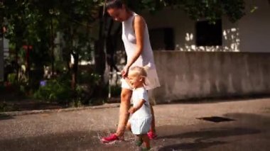 Little girl with her mom holding hands, run through the puddles and splash. High quality 4k footage