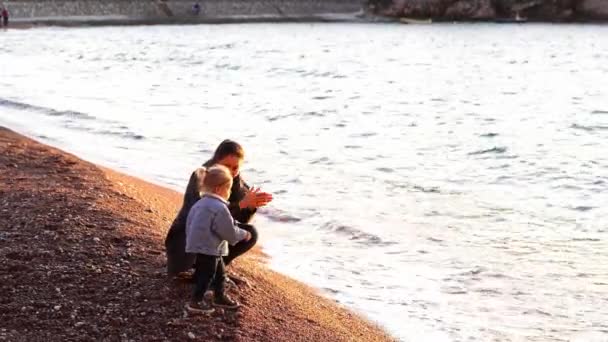Pikkutyttö Heittää Kiviä Mereen Seistessään Rannalla Äitinsä Vieressä Taputtamassa Käsiään — kuvapankkivideo