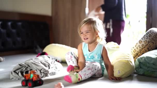 Маленька Дівчинка Сидить Ліжку Кросівками Руках Мати Кладе Одяг Шафу — стокове відео