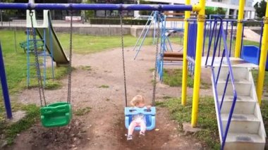 Little girl swings on a swing at the playground by the road. High quality FullHD footage