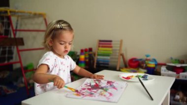 Little girl draws with a brush on paper at the table. High quality 4k footage