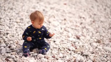 Small baby sits on a pebble beach, swarms in the pebbles and pulls it into his mouth. High quality 4k footage